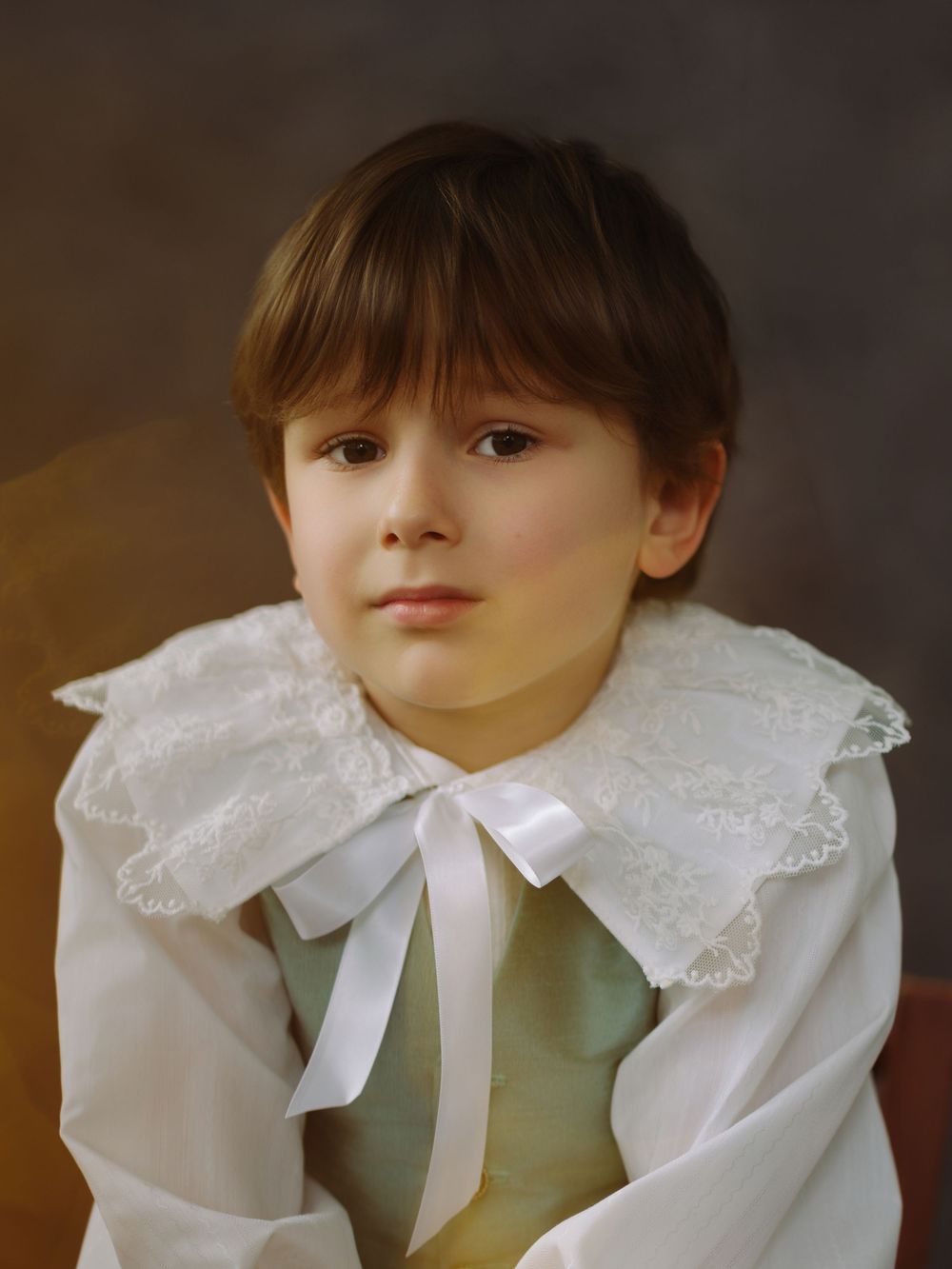 Young child in vintage white lace collar with ribbon bow, posed for a classic portrait-style photo.