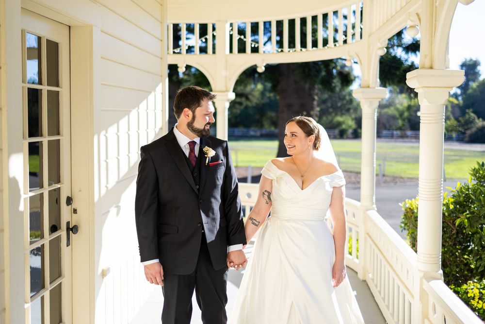 Wedding couple shares an intimate moment on a white porch with elegant columns and sunlit surroundings.