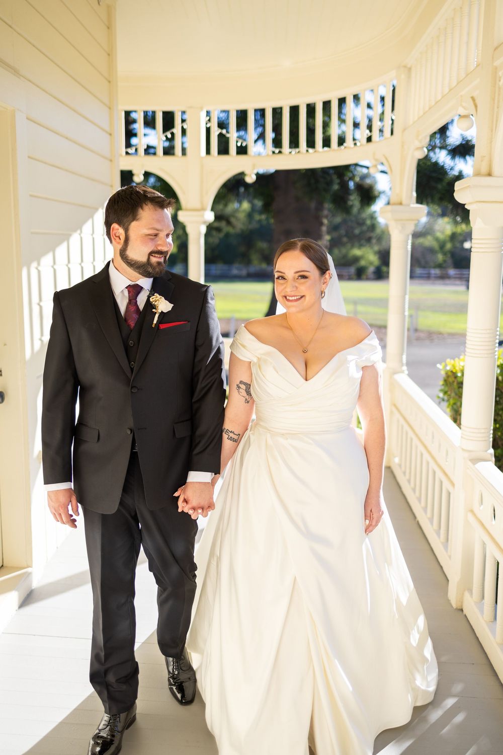 A couple walks together along a charming white porch during their wedding day.