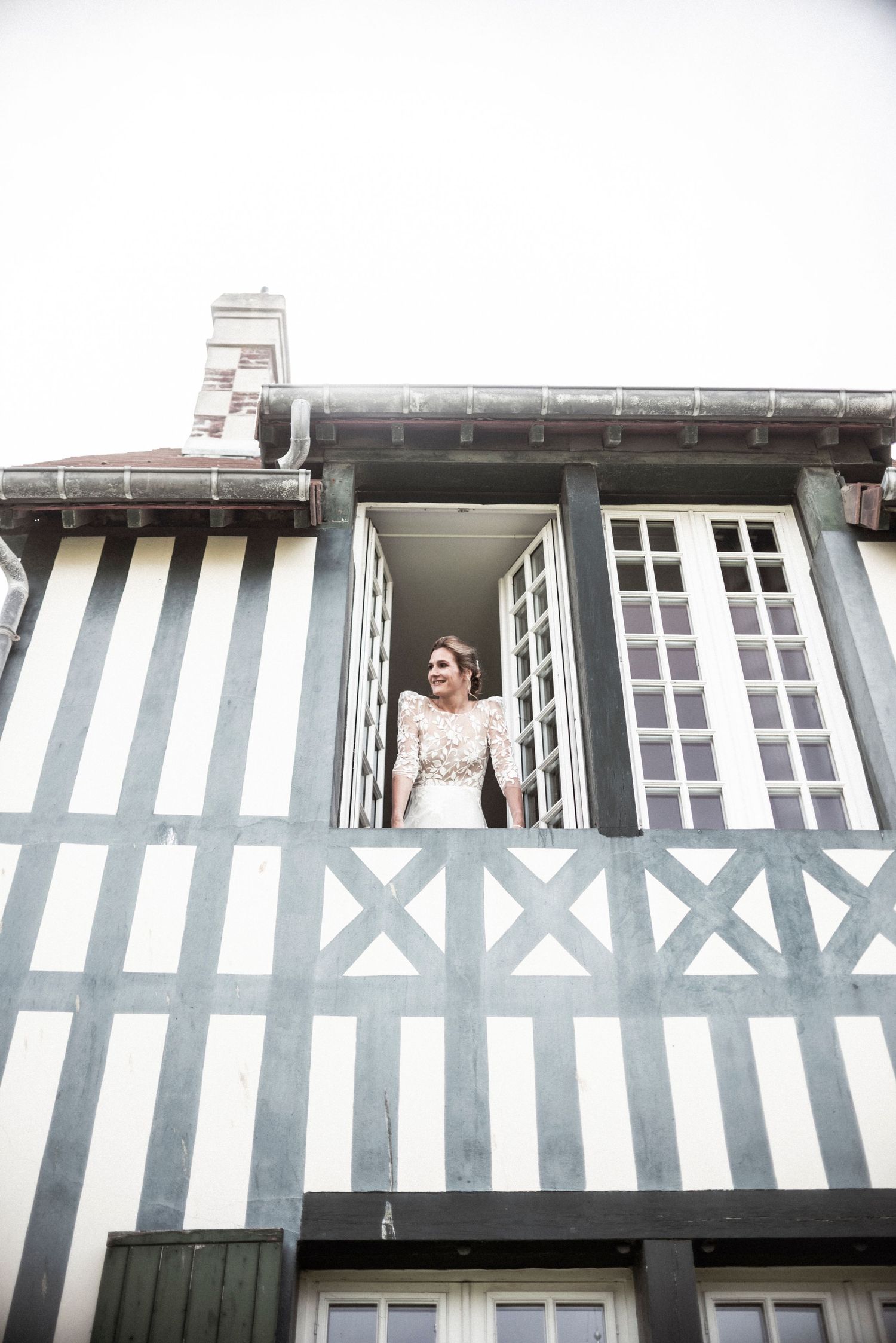 Traditional half-timbered house with white and gray facade features an ornate balcony window with classic architectural details.