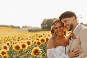 Smiling bride and groom posing together in front of a sunflower field.