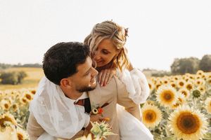 Couple embracing in a sunflower field, bride on groom's back, sharing a joyful moment in golden light.