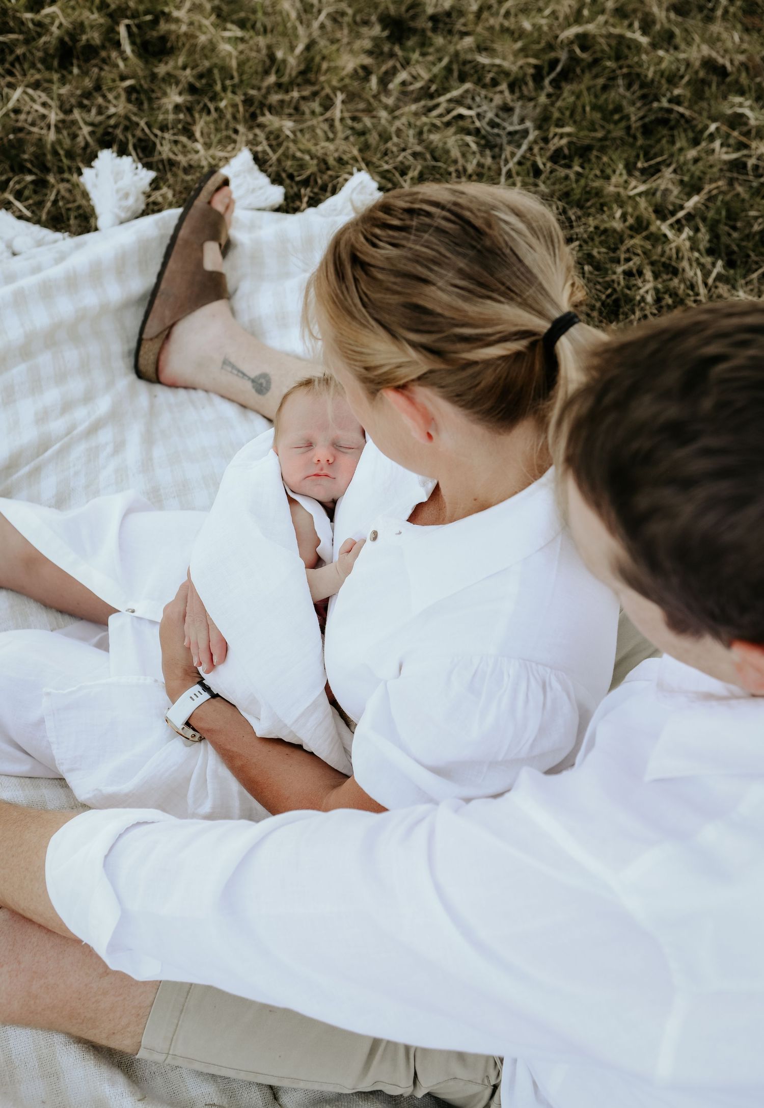 A family wearing white clothing rests together peacefully on white bedding in a tender moment.
