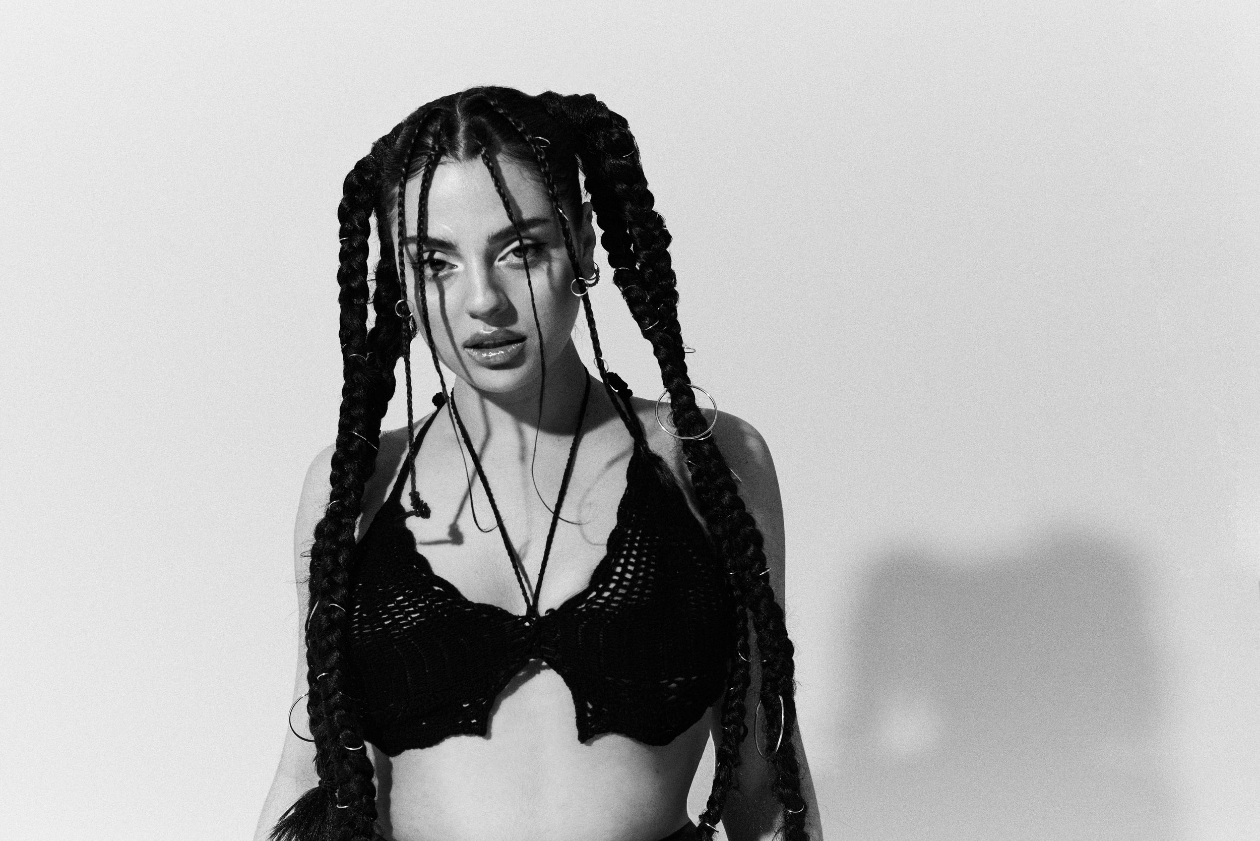 Black and white photo of woman with long box braids wearing black crop top posing confidently.
