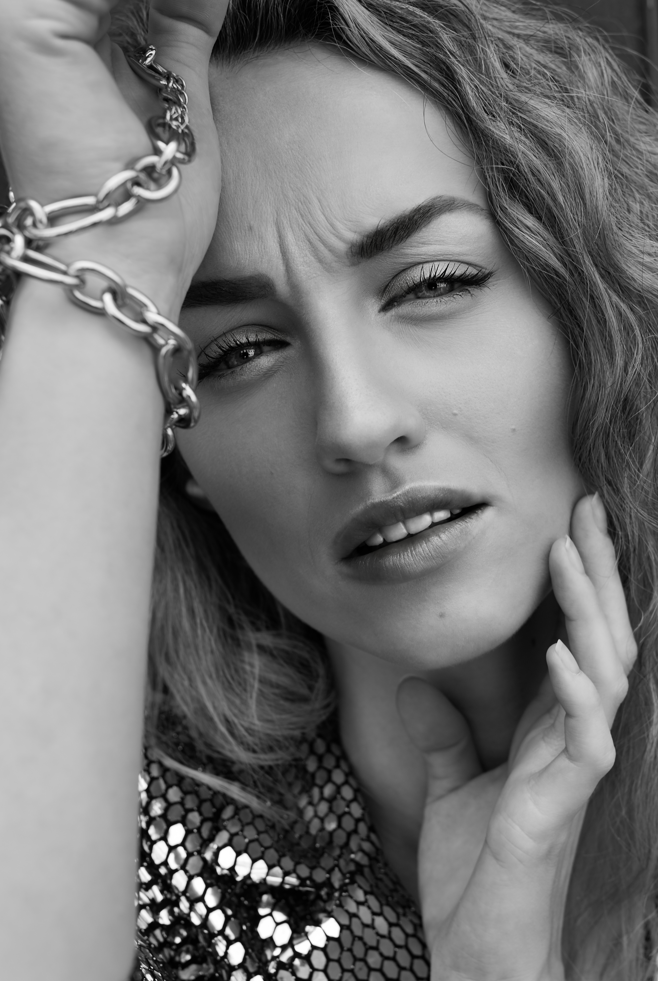 Close-up black and white portrait of a woman with a chain bracelet and sequined top.