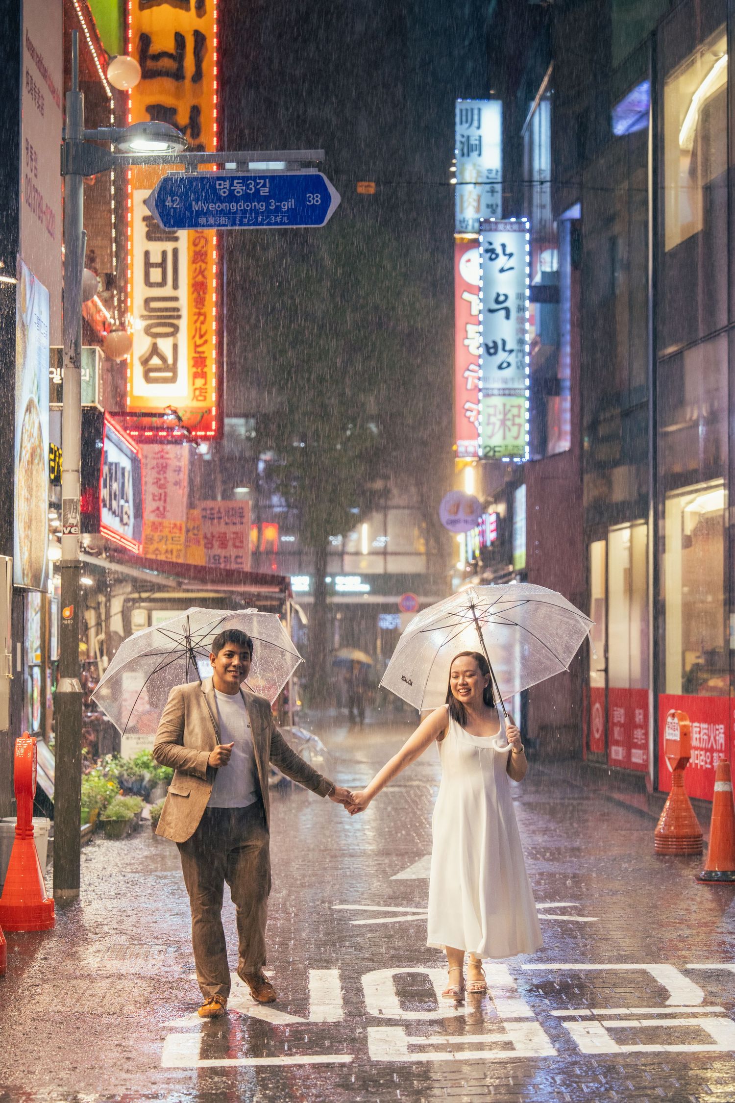 A couple with umbrellas holds hands on a rainy night in a neon-lit street in South Korea.