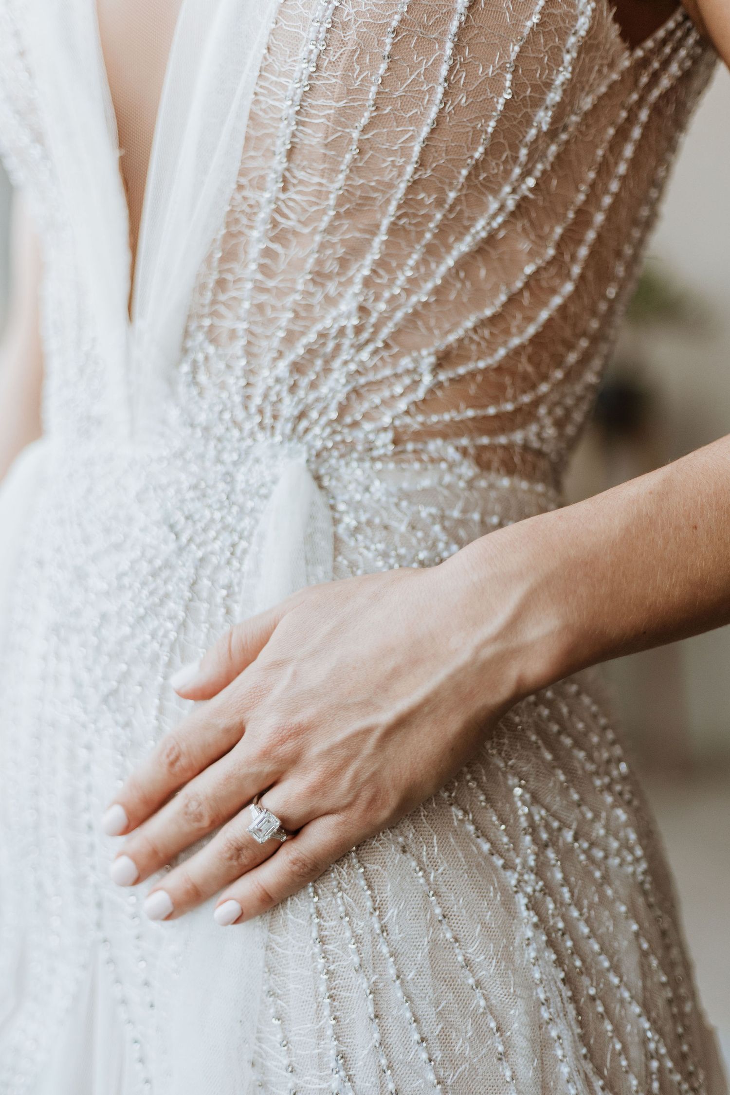 Close-up of intricate beaded details on a wedding dress bodice with an engagement ring visible.