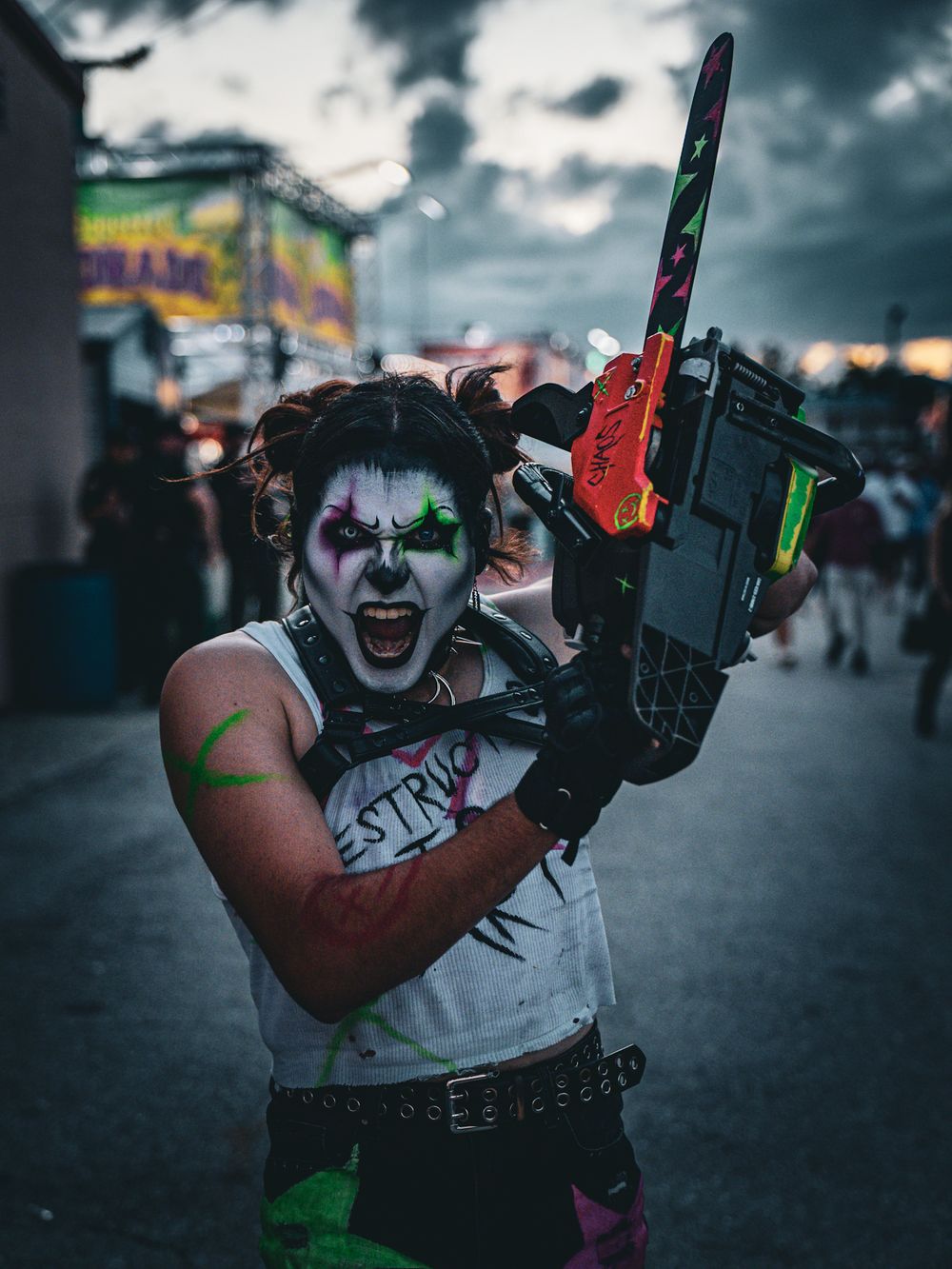 Creepy clown figure holding chainsaw prop at night carnival event.