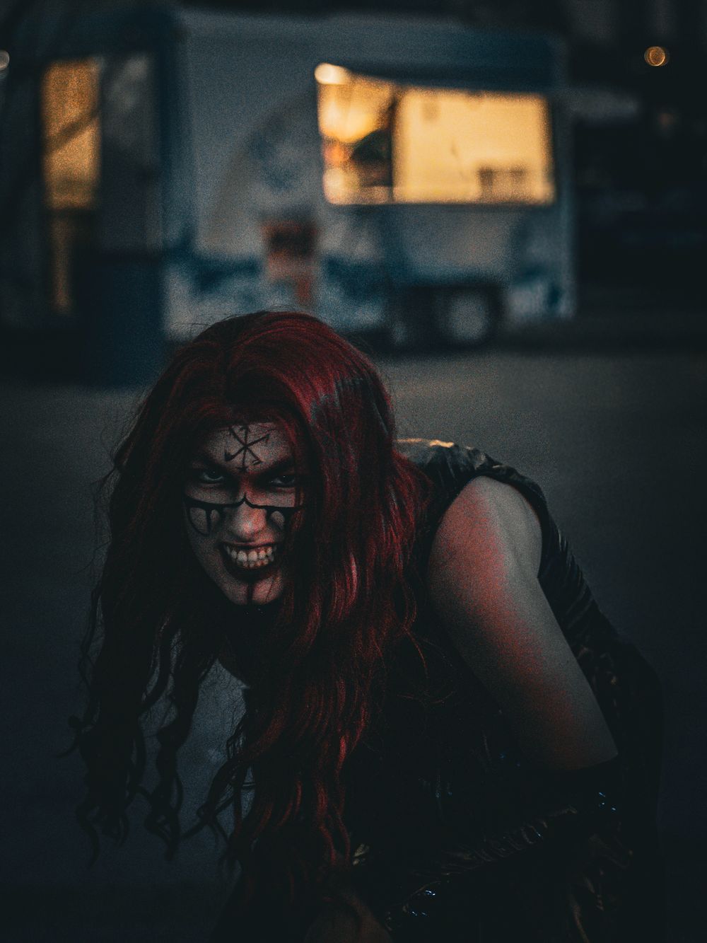 Dark and moody portrait of scary clown figure with red hair in nighttime urban setting.