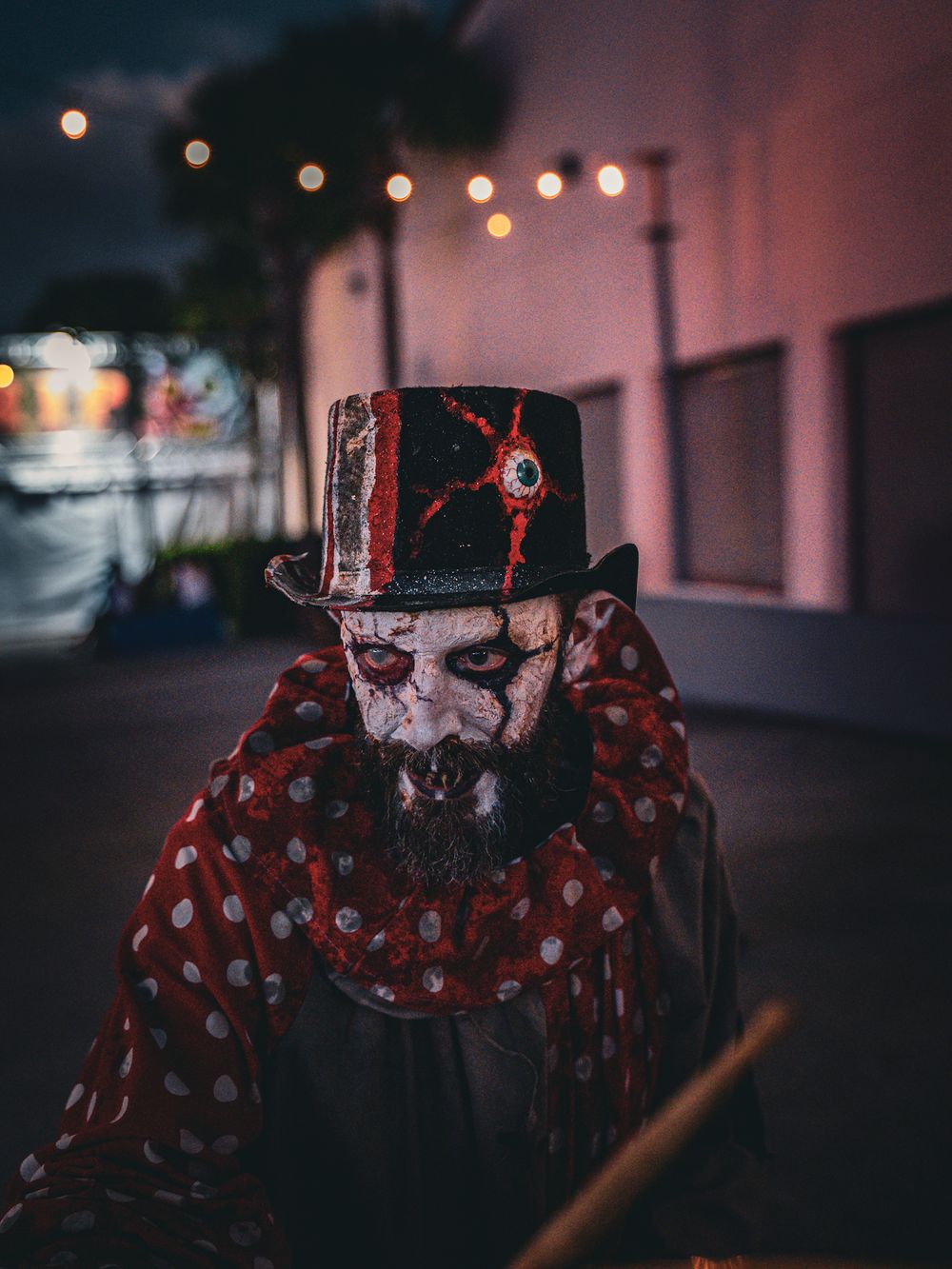Sinister clown character wearing top hat and polka dot scarf in dimly lit nighttime scene.