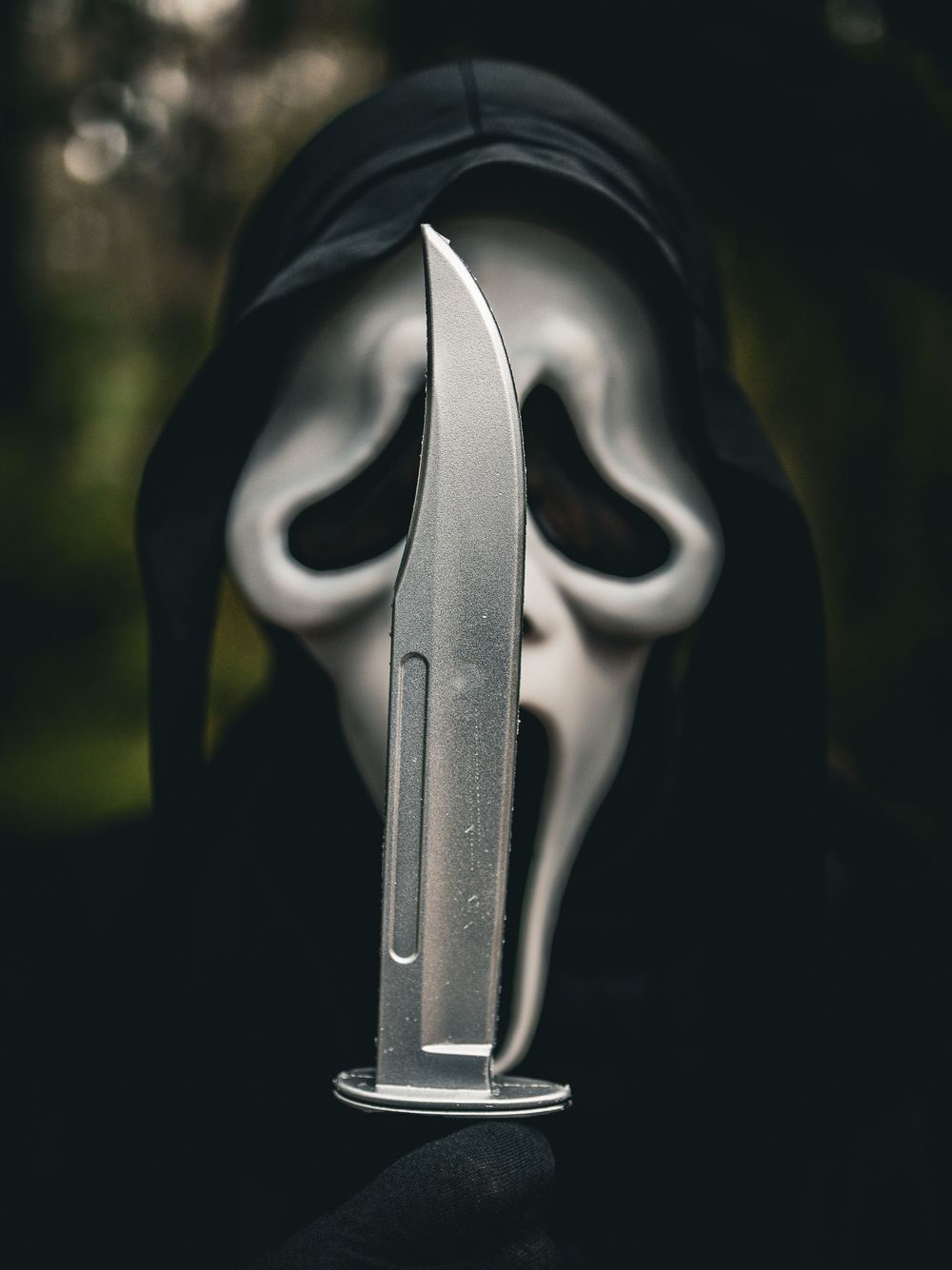 Close-up profile view of ghost mask with knife reflecting light against dark background.