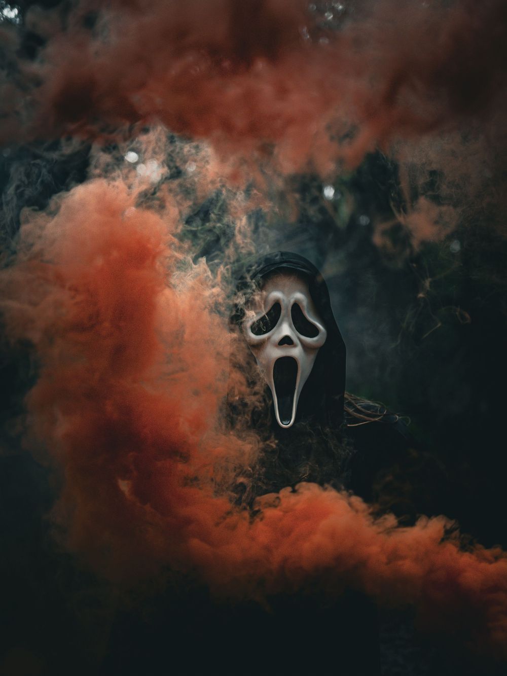 Ghostface mask emerges from dramatic orange and black smoke clouds in an eerie Halloween scene.