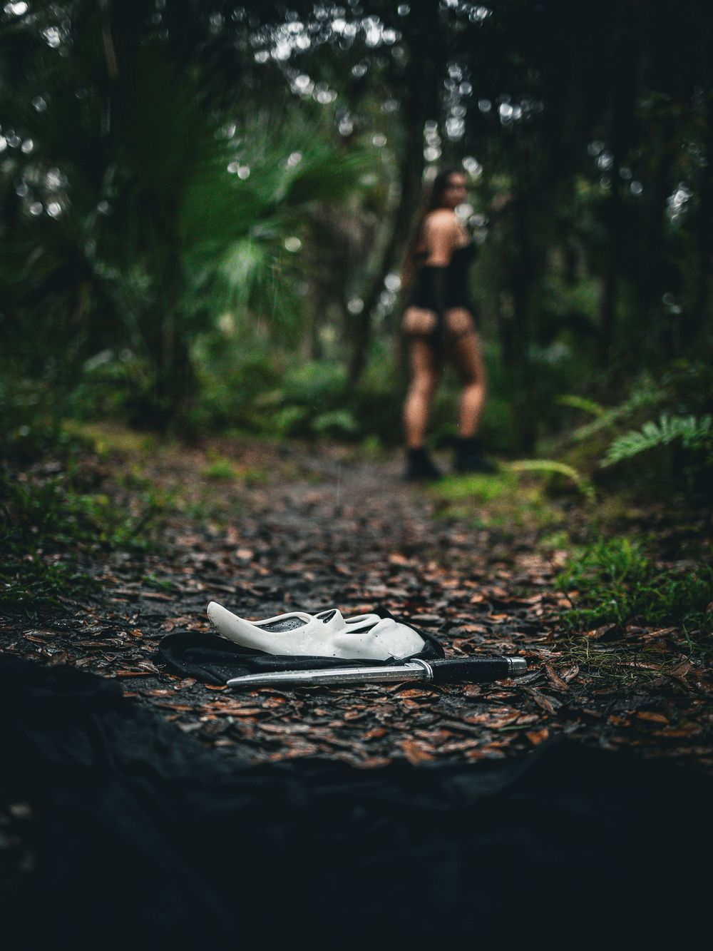 Abandoned white shoe on forest path with blurred figure in background.