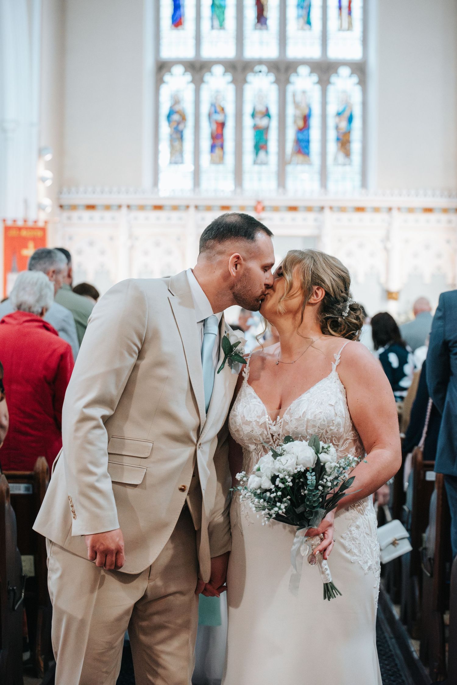 Wedding ceremony in a church with beautiful stained glass windows and traditional wooden pews.