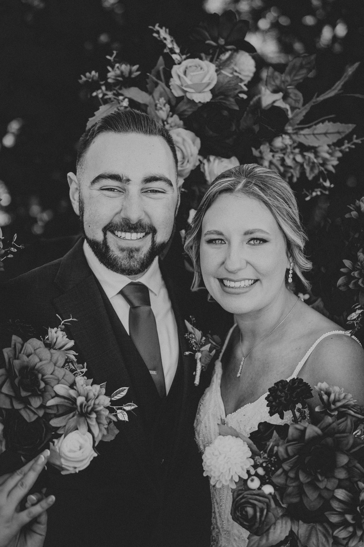 Black and white wedding photos showing joyful moments between newlyweds surrounded by flowers and greenery.