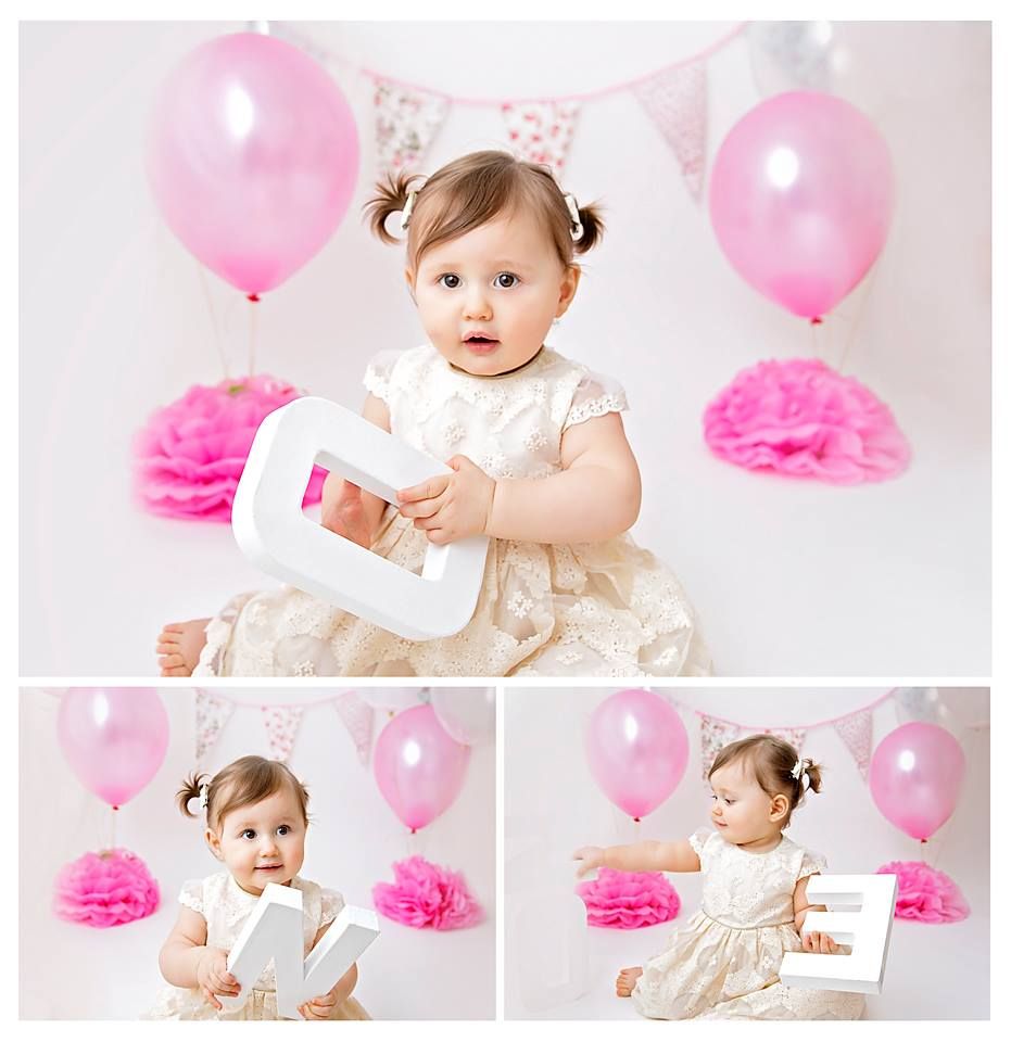 Indoor cake smash photo session with pink balloons, tissue pom poms, and white backdrop.