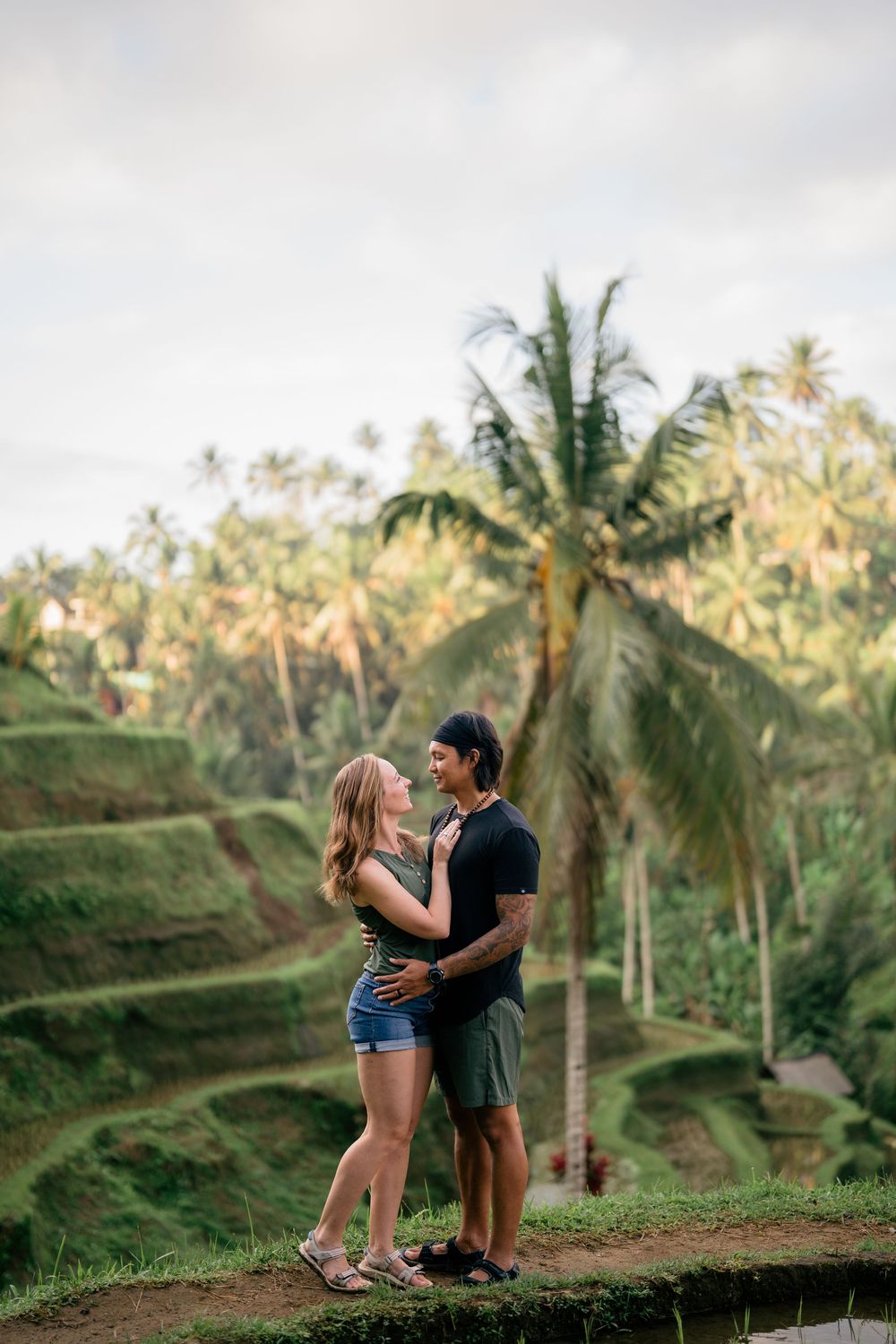 Romantic couple embracing on Bali rice terrace with palm trees in background.