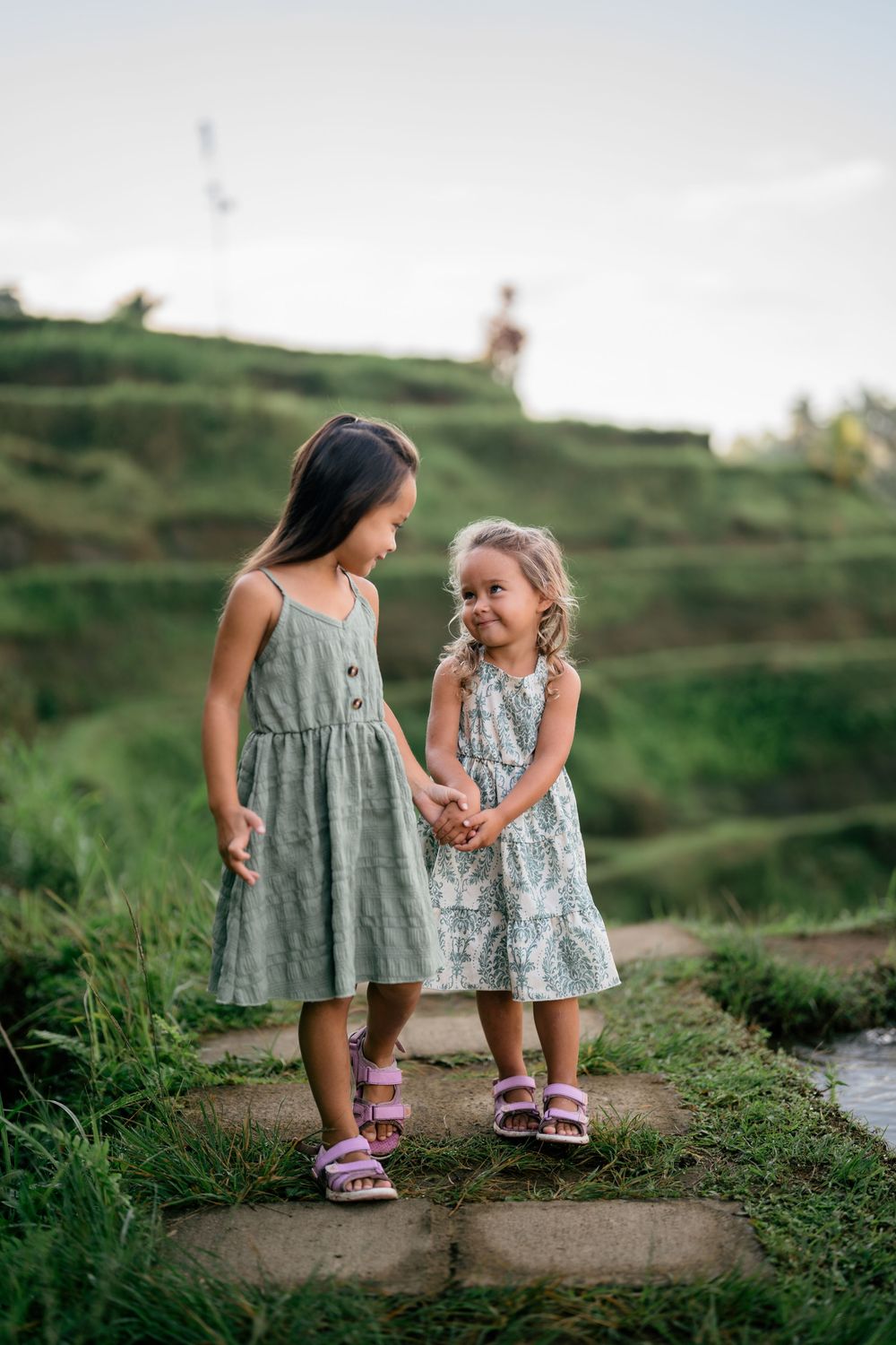Two children in matching dresses share a sweet moment on a stone path.