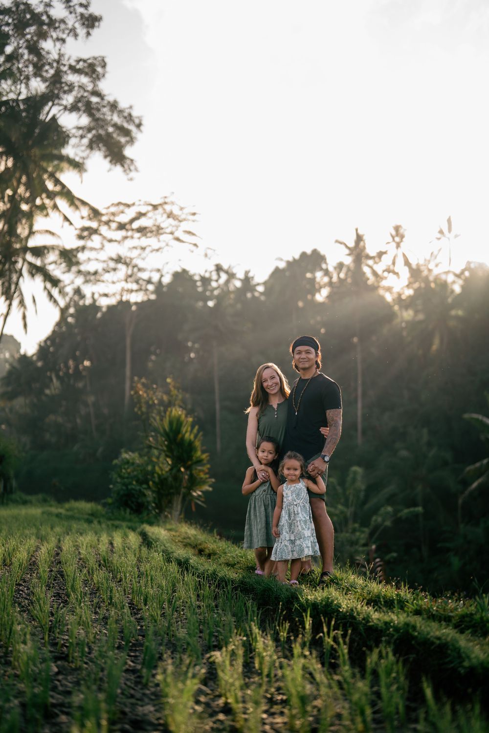 Family of four poses together at sunset on a grassy tropical hillside.