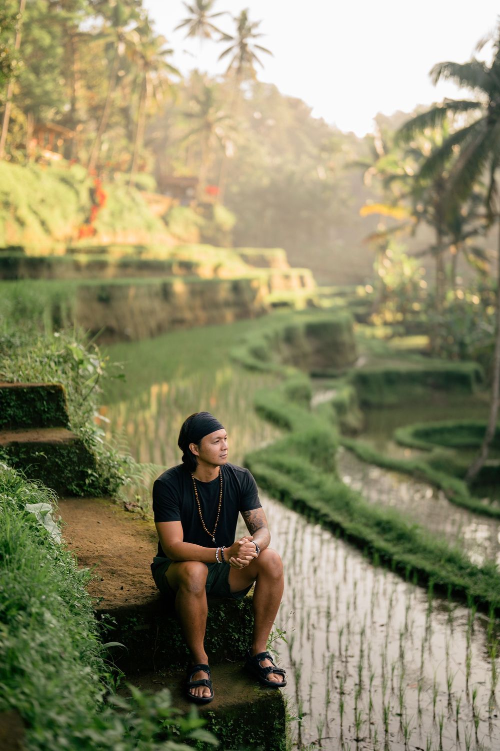 Person in black shirt sits contemplatively on rice terrace steps in Bali.