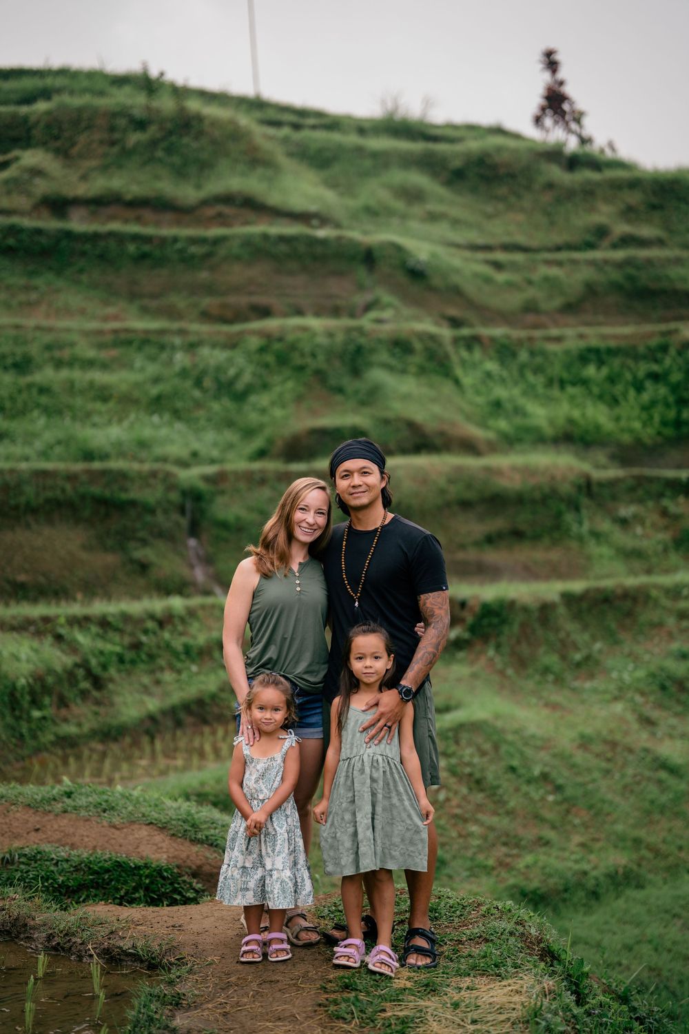Family standing together on a green terraced hillside path in a tropical setting.