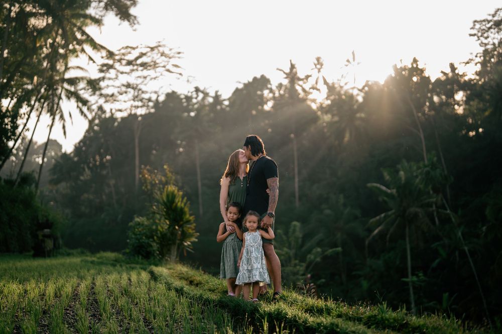 Family portrait silhouetted against sunset in tropical forest setting.