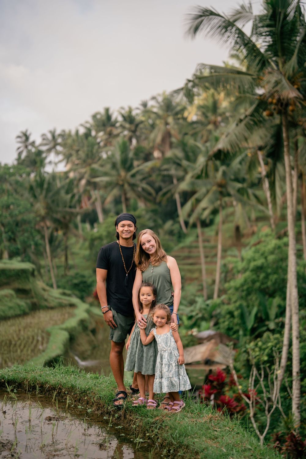 Family standing together on rice terrace path surrounded by palm trees in Bali.