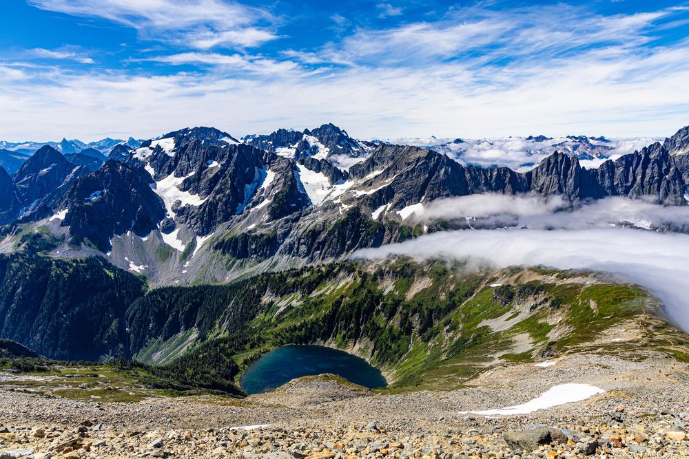 Mountain range view on a partly cloudy view with rocky slope leading down to a lake.