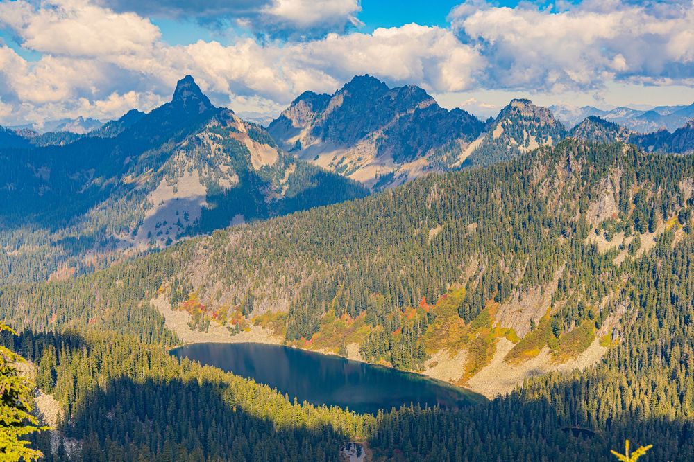 Mountain peaks and lake under partly cloudy sky casting shadows across the landscape.