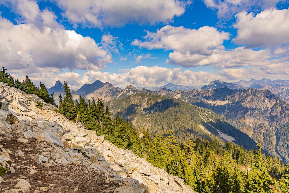 Mountain range with rocky trail in the foreground under partly cloudy skies.