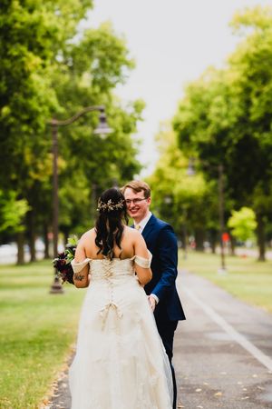 A couple shares a joyful first look moment on a tree-lined pathway in a park setting.