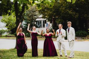 Wedding party in burgundy dresses and gray suits poses outdoors in a garden setting.