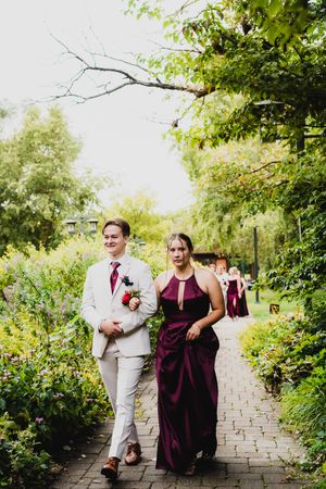 Wedding party members walk along a stone path surrounded by lush green gardens.