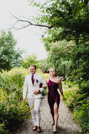 A couple walks together down a stone garden path surrounded by lush greenery and trees.