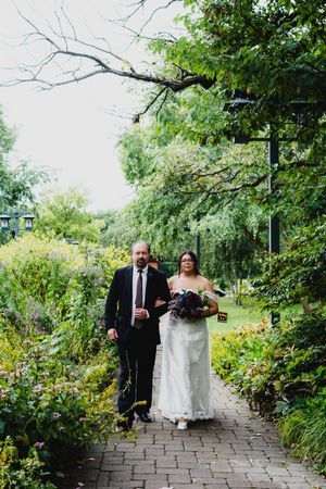 Wedding couple walks along a stone path surrounded by lush green gardens.