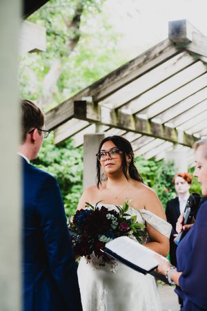 Outdoor wedding ceremony under a wooden pergola surrounded by lush greenery.