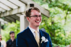 Wedding party members share laughter during outdoor photos under a pergola.