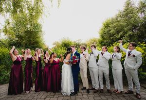 Wedding party lineup on stone path with burgundy dresses and gray suits.