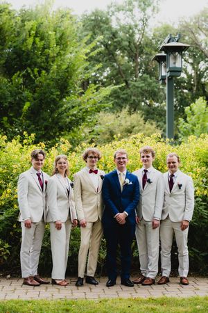 Groomsmen in white and navy suits posing together in a garden setting with yellow flowers and lamp posts.
