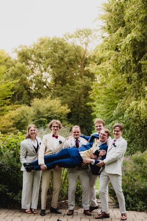 Groomsmen in light suits strike a playful pose on stone steps outdoors.