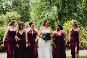Bridesmaids in deep burgundy dresses pose together in an outdoor garden setting.