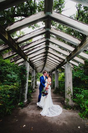 A couple poses under a dramatic pergola walkway surrounded by lush greenery.