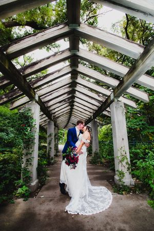 Architectural wedding portraits taken under a white pergola surrounded by green foliage.