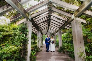 Wedding couple stands beneath an architectural pergola with geometric shadows.