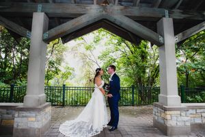 A couple in wedding attire shares an intimate moment under a covered stone patio surrounded by greenery.