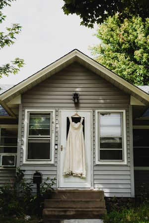 A white wedding dress hangs outside a gray house with white trim windows.