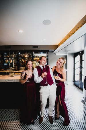 Wedding party celebrates with drinks in modern bar space with black and white tile flooring.