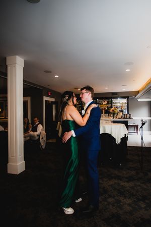 A couple dances together at an indoor venue, with the woman wearing an elegant emerald green dress and the man in navy blue.