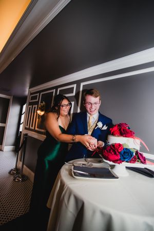 Wedding couple shares a private moment while looking at a bouquet of red flowers on a white tablecloth.