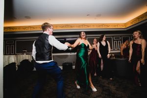 Wedding guests dance in line formation at evening reception with warm lighting.